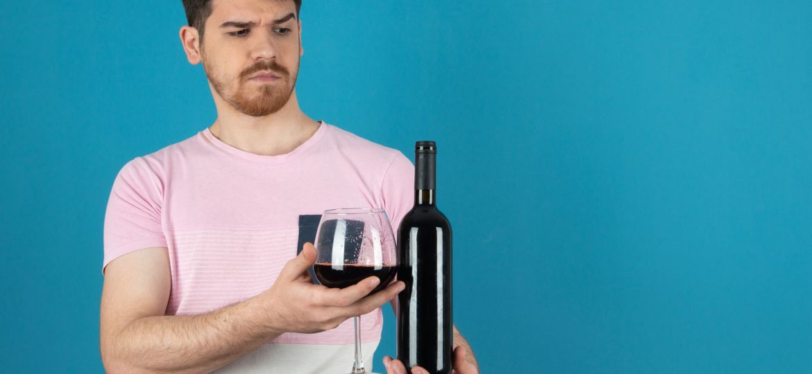 Angry handsome and holding glass of wine and bottle on a blue background